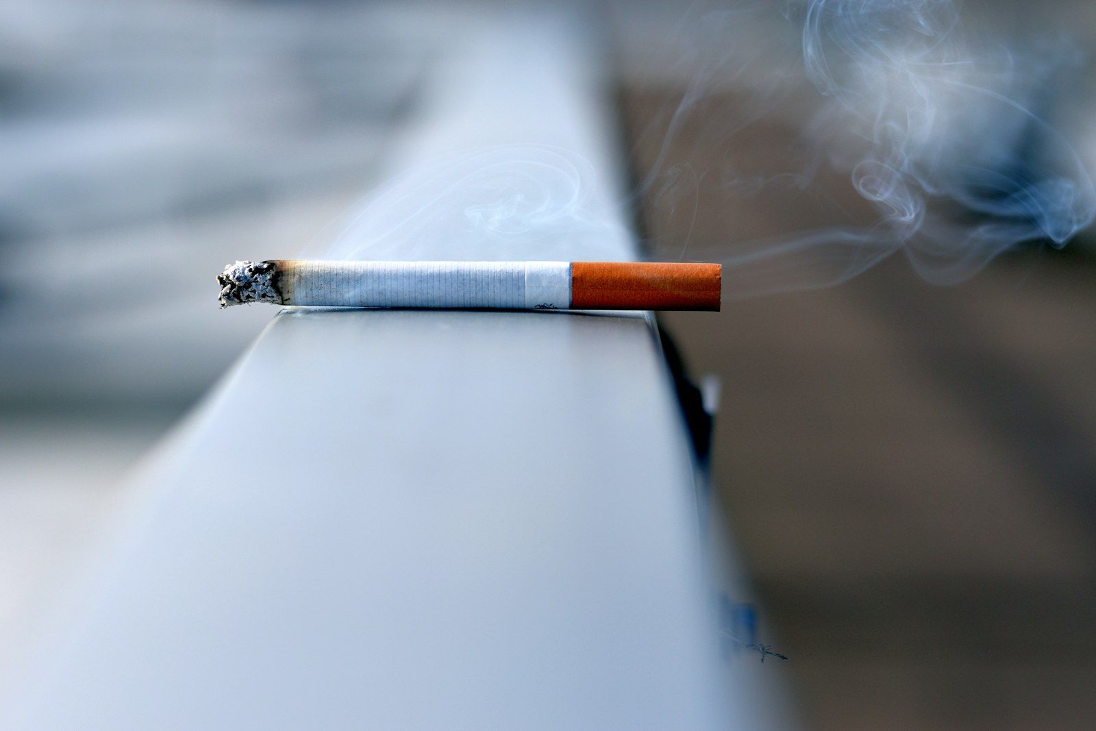 Cigarrillo encendido apoyado en una barandilla, el tabaco antes de un lifting facial